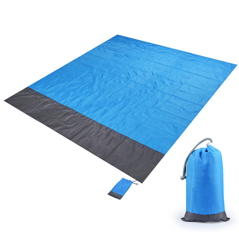 Maroon Asteria portable waterproof picnic and beach camping mat with pocket, spread on sandy surface for outdoor relaxation.