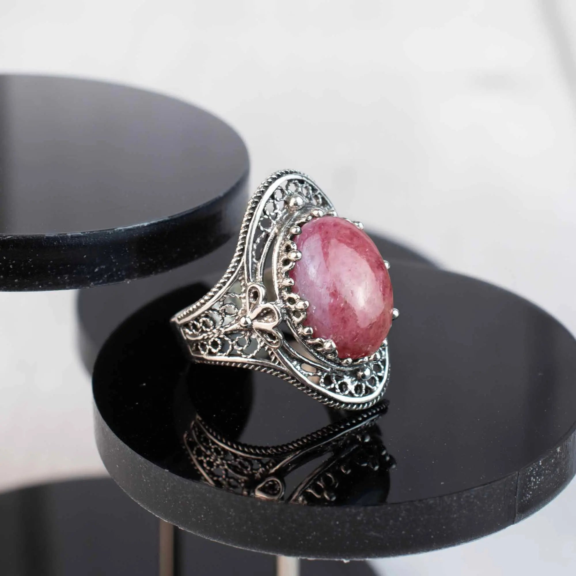 Silver statement ring featuring rhodonite gemstone with intricate filigree art design on a woman’s hand.