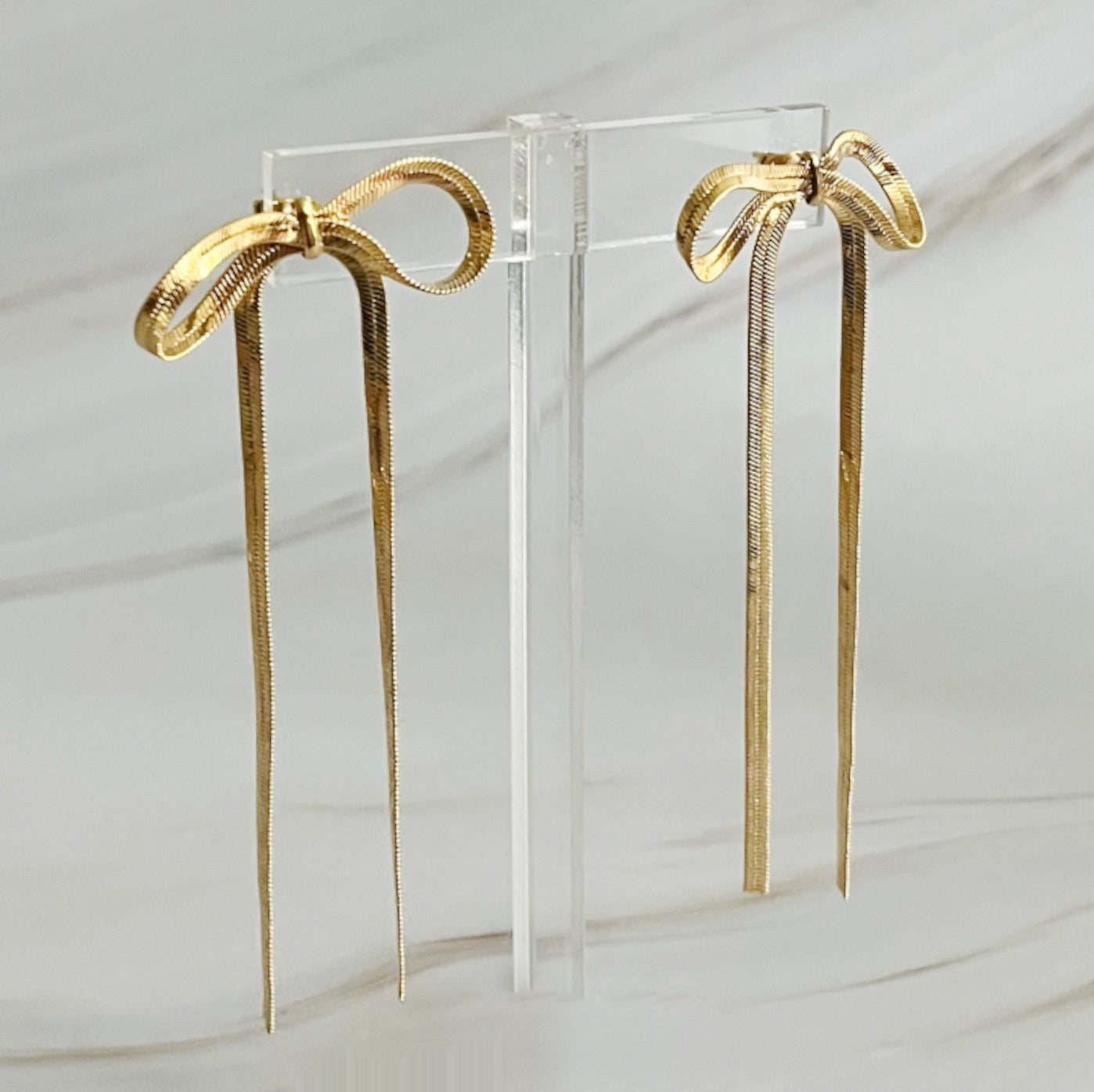 Fuchsia Hercules long drop bow earrings featuring elegant jewelry design with gold-toned bows and dangling chain details.