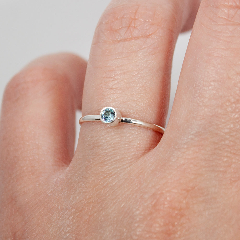 Sterling silver ring featuring a dainty blue topaz solitaire gemstone in a tube setting, elegant jewelry by Grey Clymene.