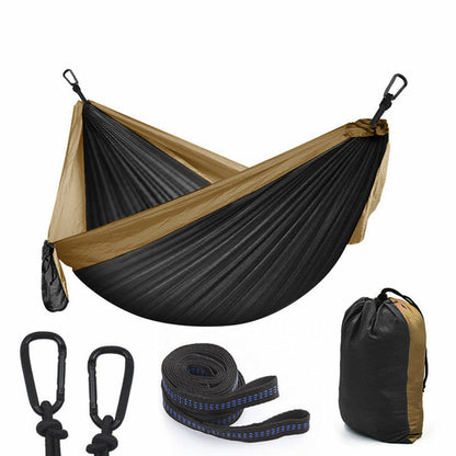 Maroon Asteria camping parachute hammock for outdoor survival, shown hanging in a garden with trees and greenery.