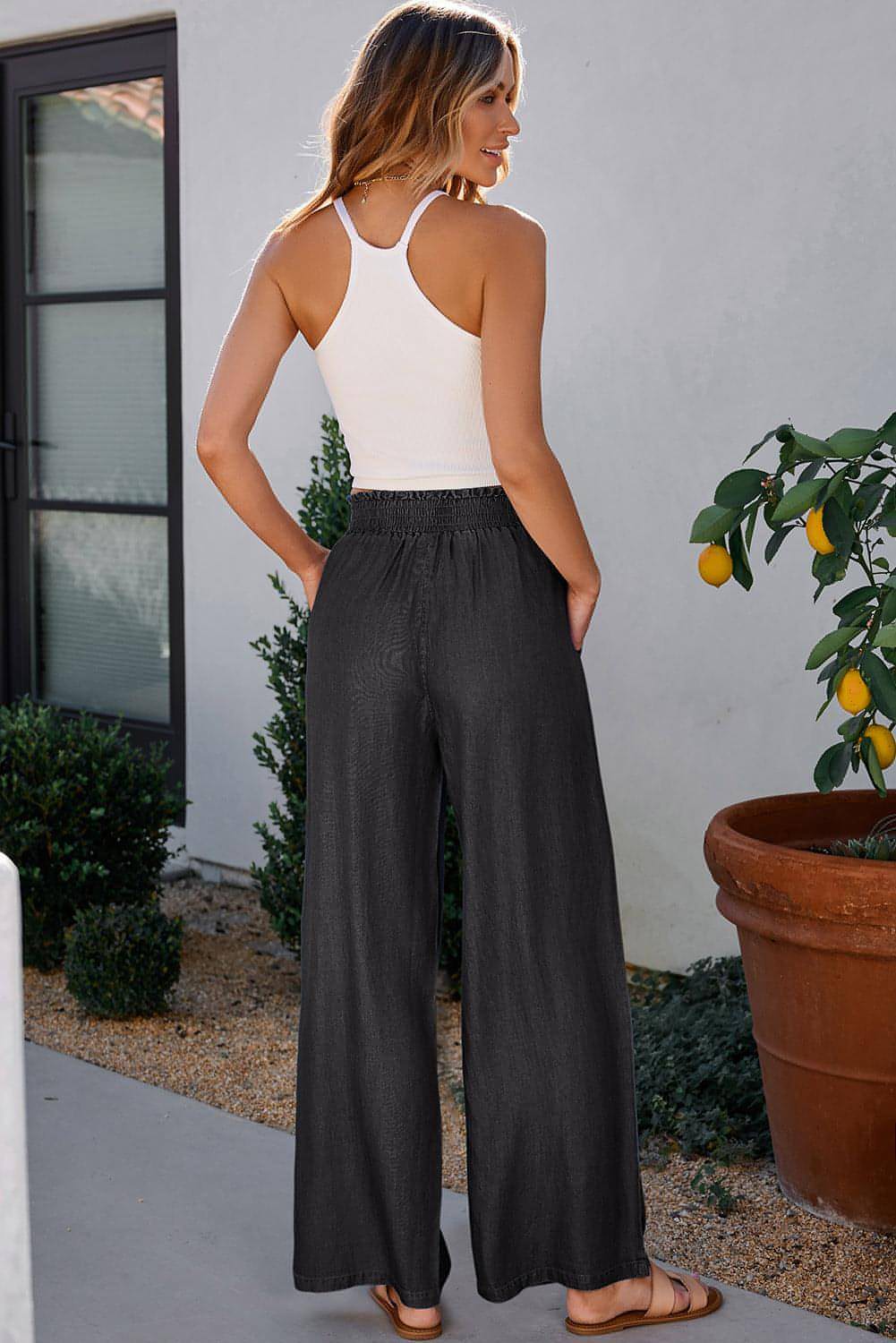 Black high waist wide leg jeans with side pockets, frilled details, and smocked waistband by Carmine Juneberry.