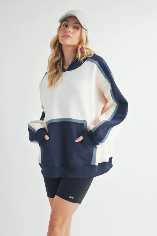 Aemi + Co color block kangaroo pocket hoodie from Pear Daisy, featuring a cozy, stylish design with a front pocket and vibrant color blocks.