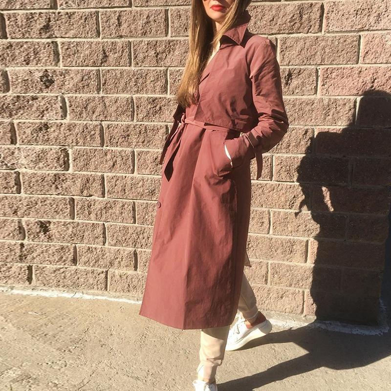 Women’s long brick red trench coat by Jade featuring a V-neck, tied waist, windbreaker style, and lightweight jacket design.
