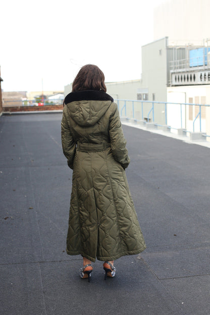 Olive green quilted single-breasted longline hooded coat by Rose Eleusis, displayed on a hanger with a button closure and padded design.