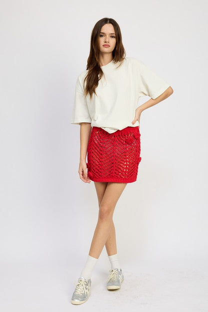 Crochet mini skirt with rosette details by Jade Icarus, shown in a close-up of the textured crochet fabric and floral accents.