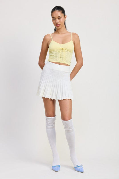Jade Icarus pleated mini skirt with automotive-inspired design, displayed on a model in a modern setting.