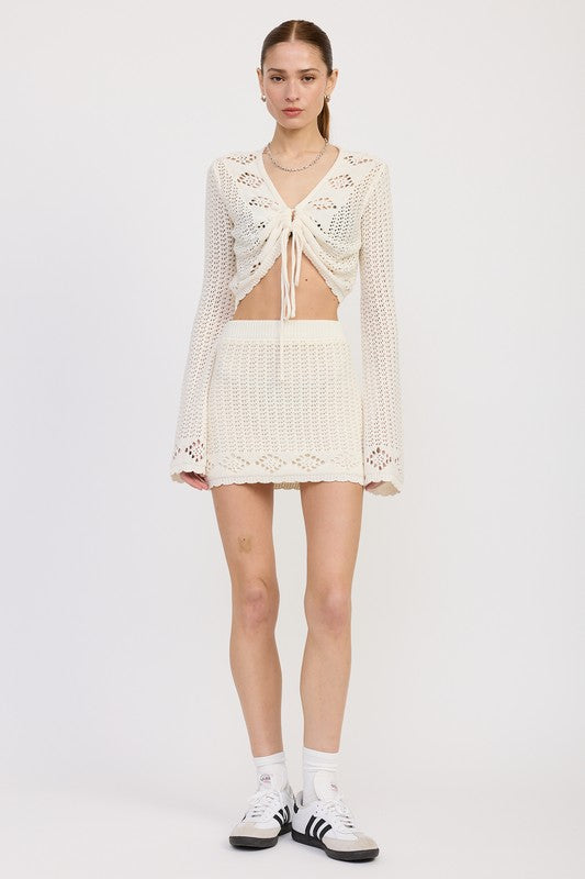 Jade Icarus lettuce hem mini crochet skirt shown on a model, featuring a textured crochet pattern and lettuce hem detail.