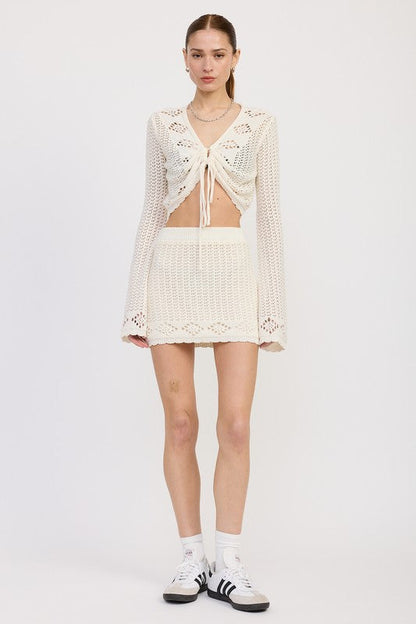 Jade Icarus lettuce hem mini crochet skirt shown on a model, featuring a textured crochet pattern and lettuce hem detail.