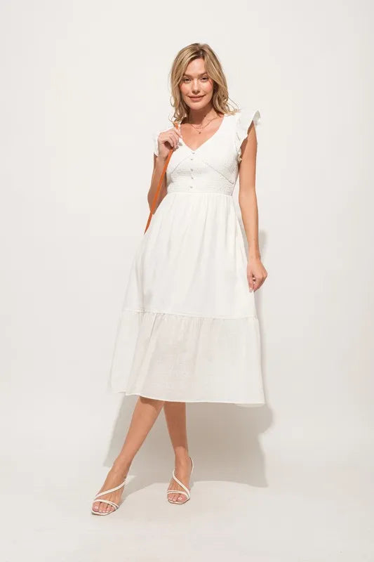 Pear Daisy ruffle sleeve front smocked tiered midi dress hanging in a home setting, showcasing its feminine design and tiered skirt.