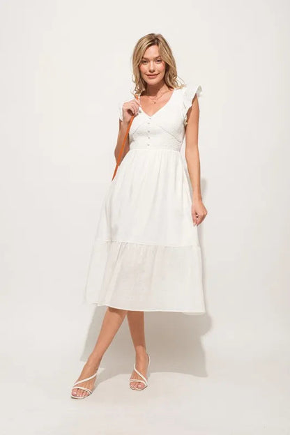 Pear Daisy ruffle sleeve front smocked tiered midi dress hanging in a home setting, showcasing its feminine design and tiered skirt.