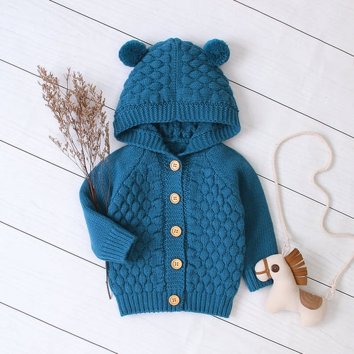 Baby wearing the Carmine Juneberry KuschelGlöckchen™ hooded knit jacket with pom-pom, cozy baby clothing for cold weather.