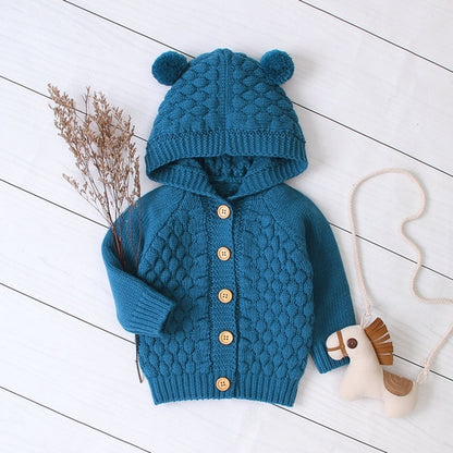 Baby wearing the Carmine Juneberry KuschelGlöckchen™ hooded knit jacket with pom-pom, cozy baby clothing for cold weather.