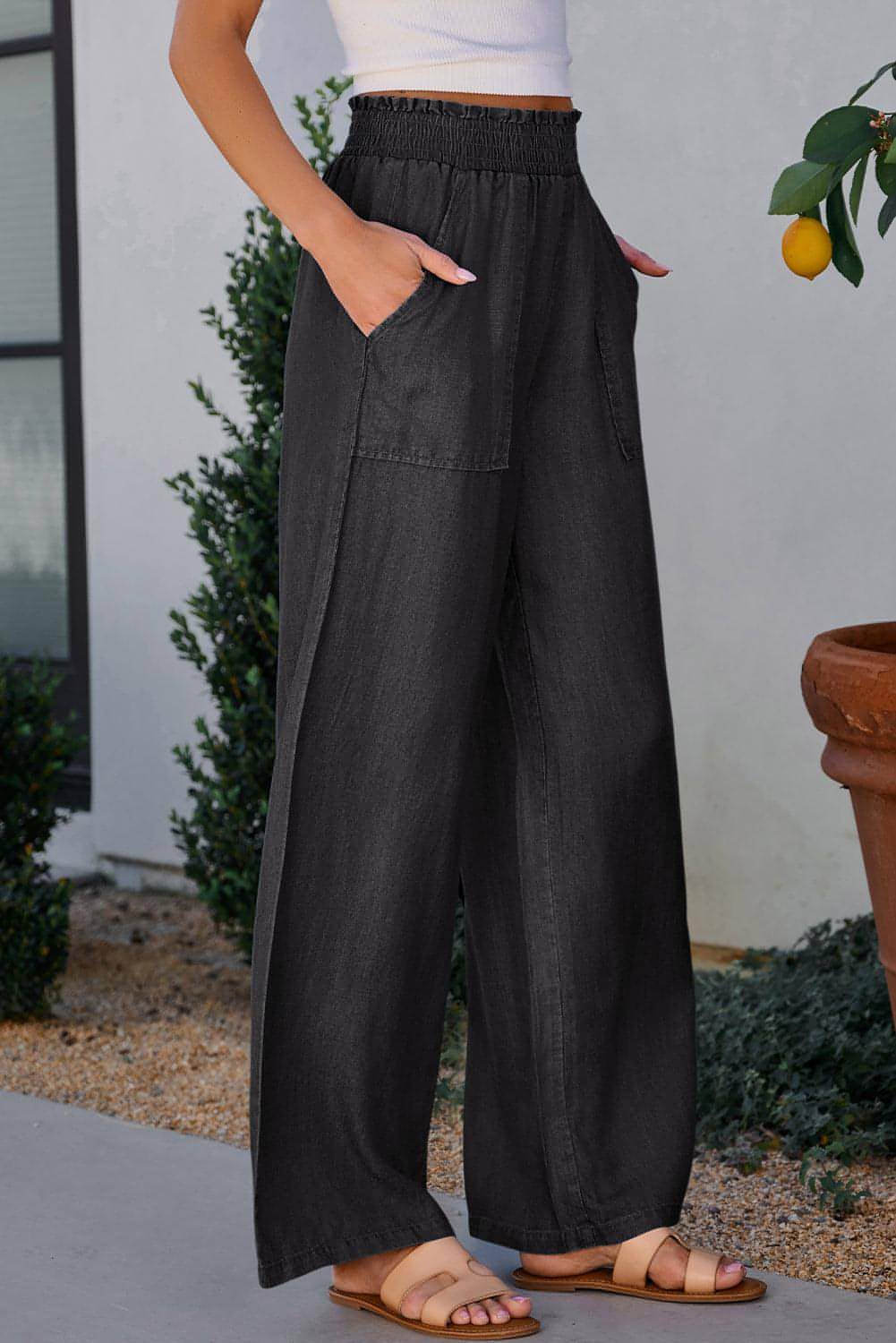 Black wide-leg jeans with frilled sides, smocked high waist, and pockets by Carmine Juneberry, shown from the side.