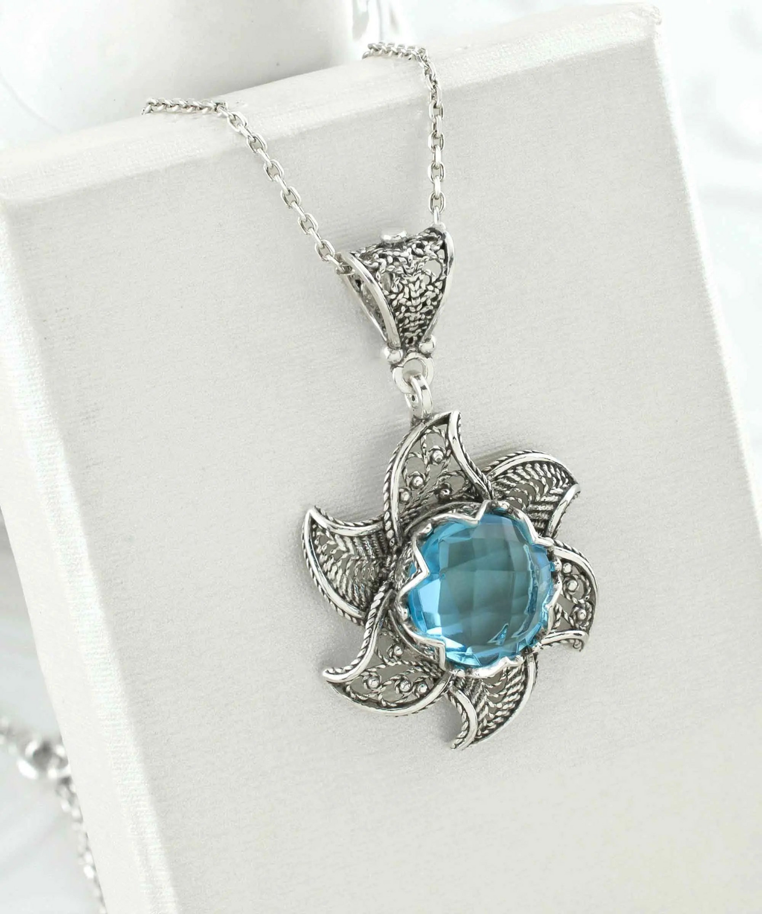 Sterling silver filigree necklace with a blue topaz gemstone blossoming lotus flower pendant, intricate jewelry design.