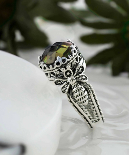 Silver cocktail ring with detailed bee and alexandrite gemstone filigree design, worn by a woman, showcasing intricate jewelry craftsmanship.