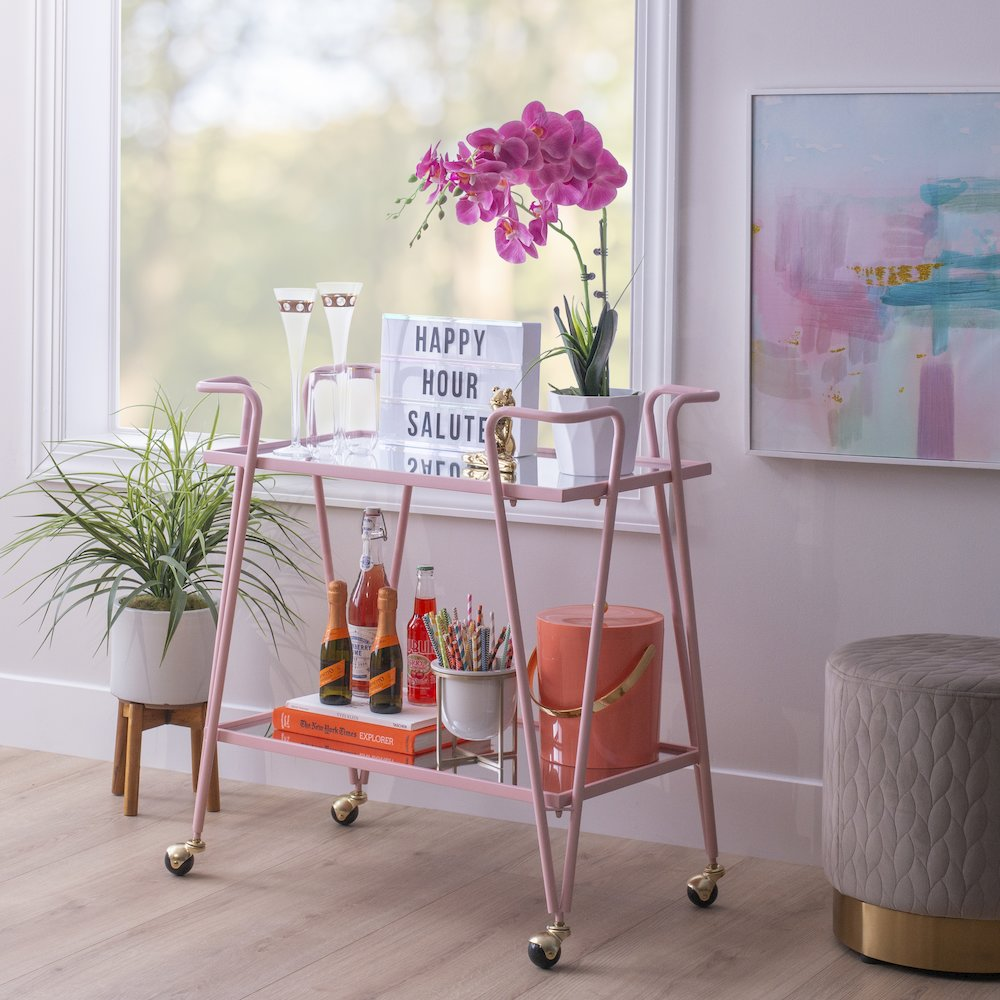 Pink mid-century bar cart from Start2Finish featuring a sleek metal frame, two shelves, and castered wheels for easy mobility.