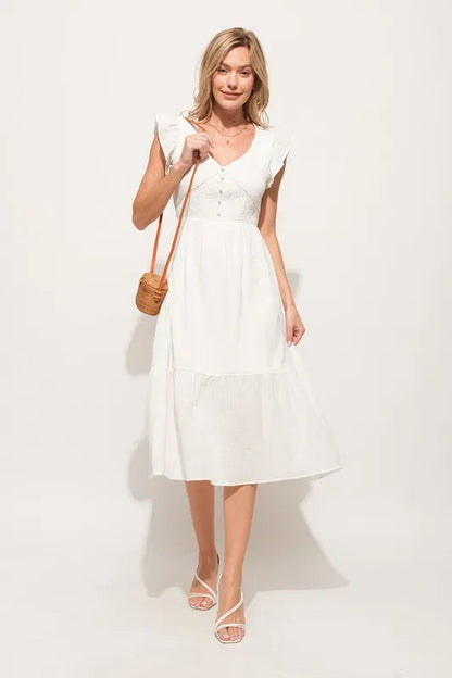 Pear Daisy ruffle sleeve front smocked tiered midi dress hanging in a home setting with floral decor.