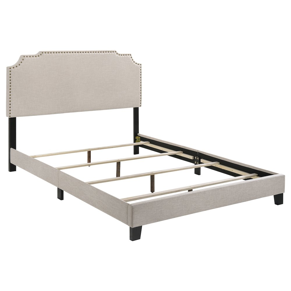 Beige Tamarac upholstered queen panel bed by Start2Finish with padded headboard and wooden frame, shown in a modern bedroom setting.