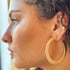 Gold Alma Thick Flattened Metal Hoop Earrings by Fuchsia Hercules, showing large, shiny gold hoops with a flattened design.