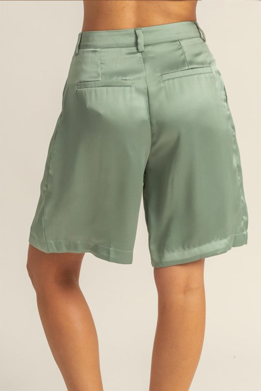 Satin high-waist pleated shorts by Jade Icarus, displayed on a model with a sleek automotive-inspired background.