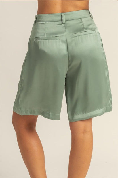 Satin high-waist pleated shorts by Jade Icarus, displayed on a model with a sleek automotive-inspired background.
