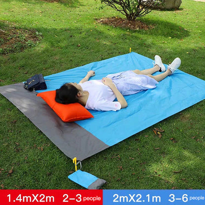 Maroon Asteria portable waterproof picnic and beach camping mat with a pocket, spread out on a grassy area.