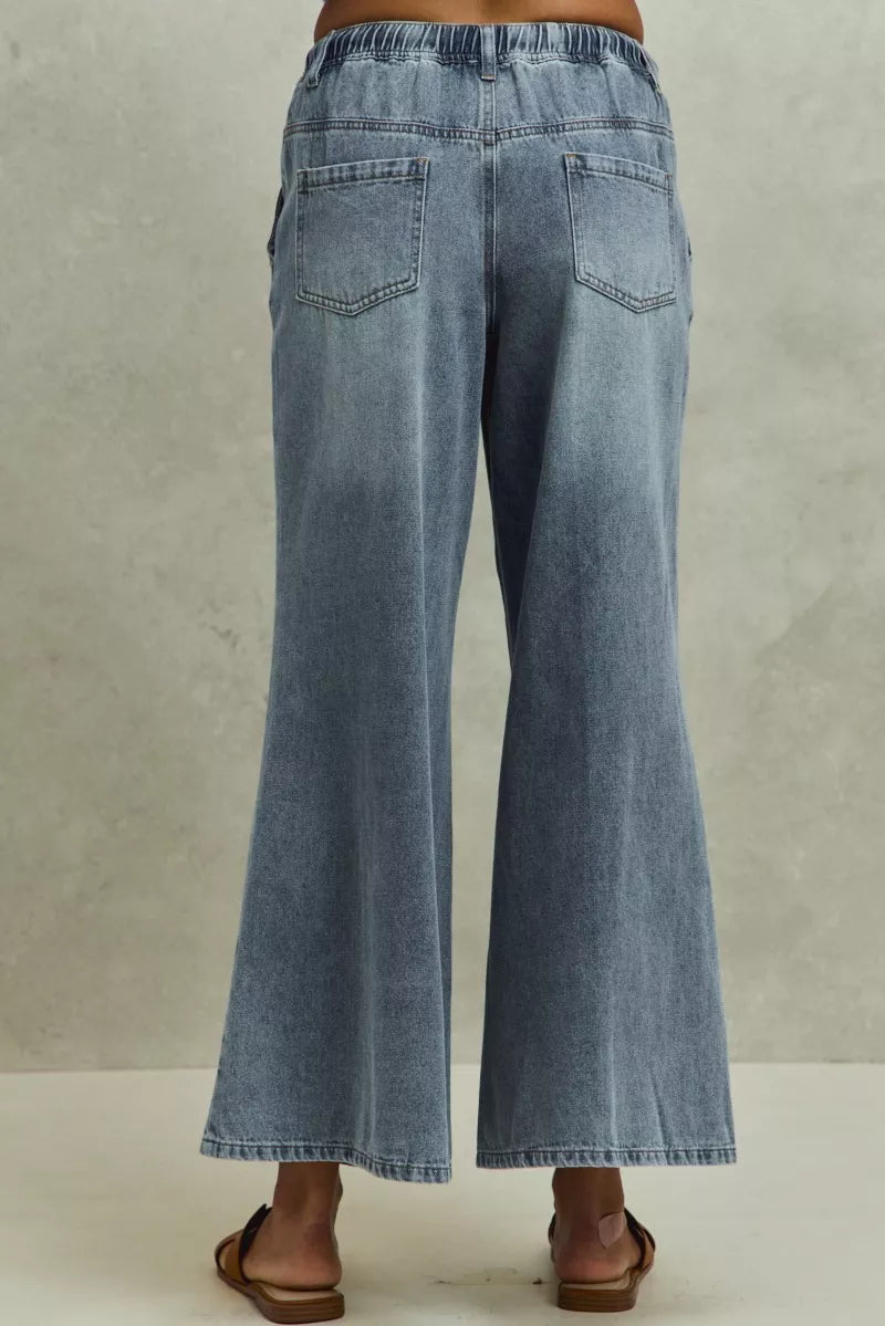 Pear Daisy SO ME mid-rise elastic waist flare denim jeans with a relaxed fit, shown on a model in a home and garden setting.