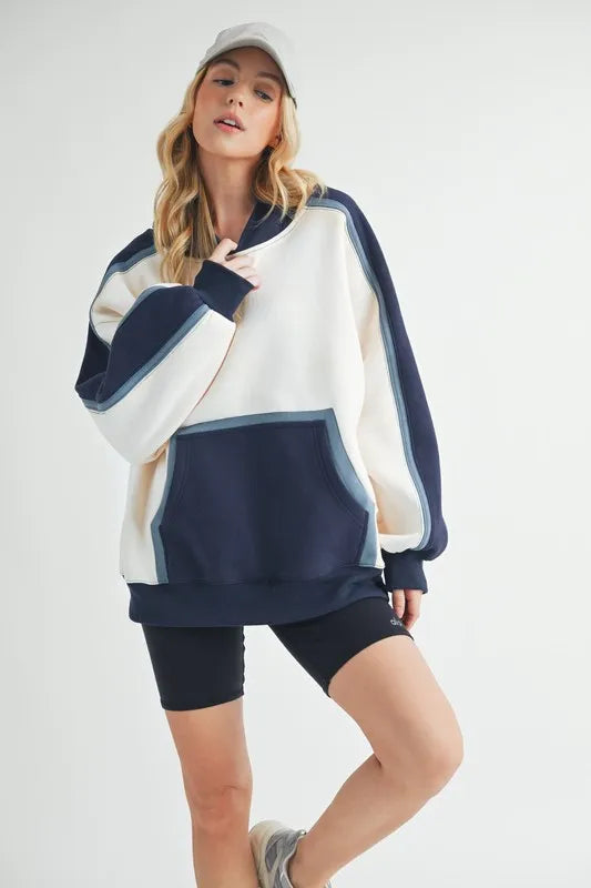 Aemi + Co color block kangaroo pocket hoodie by Pear Daisy, featuring a cozy, stylish design with a front pocket and vibrant color blocks.
