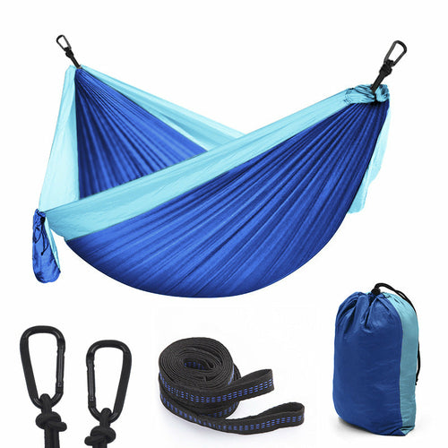 Maroon Asteria camping parachute hammock for outdoor survival, shown hanging between trees in a garden setting.