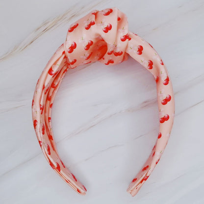 Fuchsia Hercules satin headband with cherry and bow embellishments, stylish jewelry accessory for elegant or casual wear.