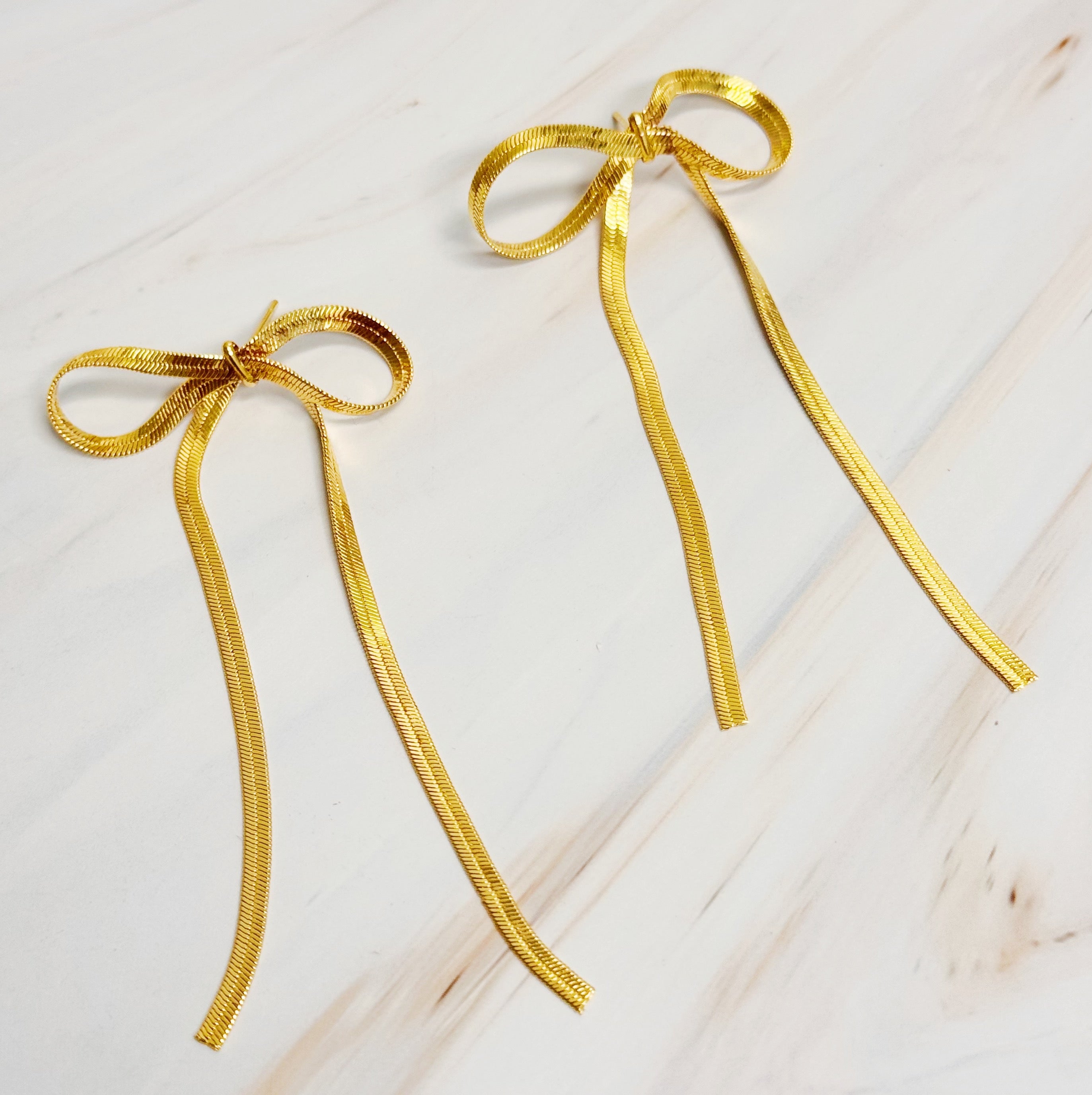 Fuchsia Hercules long drop bow earrings with elegant design, featuring delicate bow shapes hanging from thin hooks.
