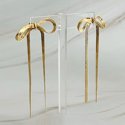 Fuchsia Hercules long drop bow earrings featuring elegant jewelry design with gold-toned bows and dangling chain details.