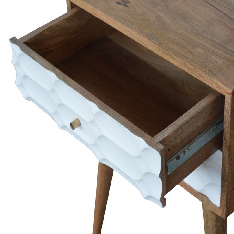 Capsule carved bedside table from Jade Epimetheus furniture with intricate detailing and a smooth finish on a modern bedroom setting.