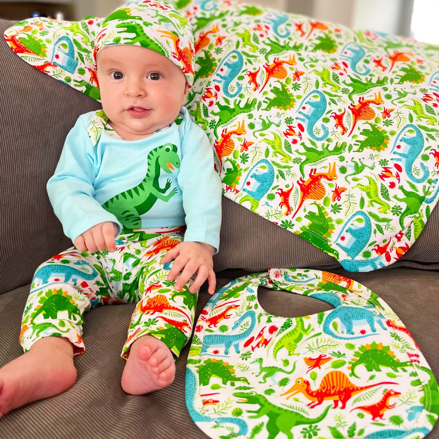 Black Simba baby layette set with dinosaur long sleeve onesie, pants, and cap for boys, featuring playful dinosaur prints.