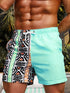 Raspberry Eurybia Hawaiian vacation beach shorts with vibrant tropical floral print and relaxed fit on a sandy background.