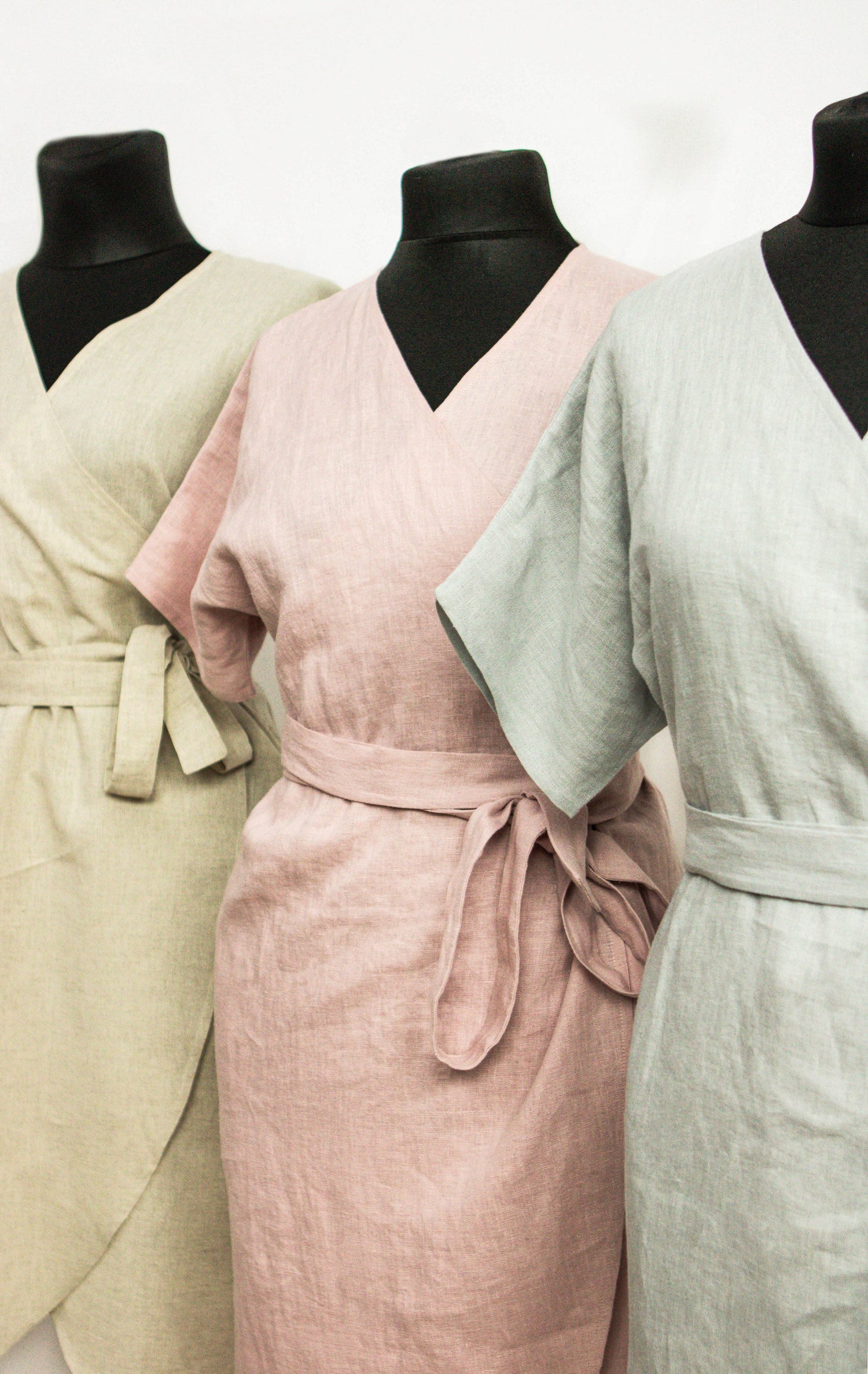 Pale pink linen wrap dress by Magenta Sugarplum featuring a fitted waist and flowing skirt, displayed on a hanger.