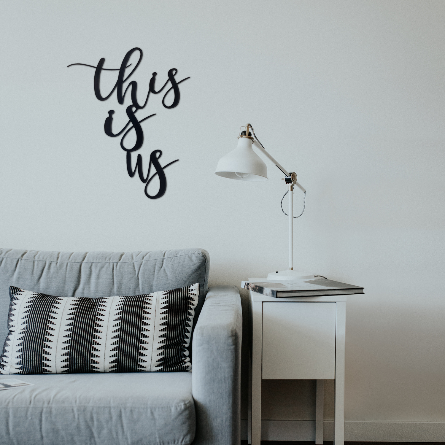 Metal wall art with "This Is Us" design by Malachite, displayed as home decor in a modern living room setting.