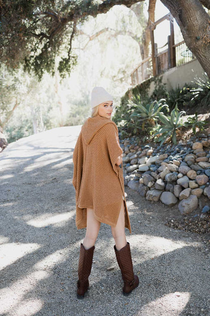 Camel-colored cozy soft waffle hooded ruana from Periwinkle Aether, draped over a chair, showcasing its textured fabric and relaxed style.