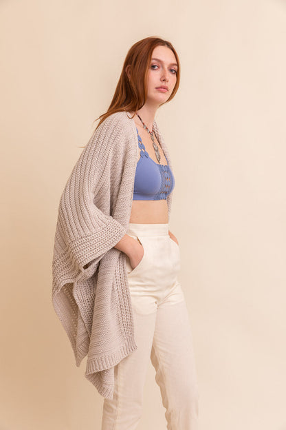 Periwinkle Aether ridged rib knit ruana, stylish layering wrap in oatmeal color, showcasing textured knit fabric and cozy drape.