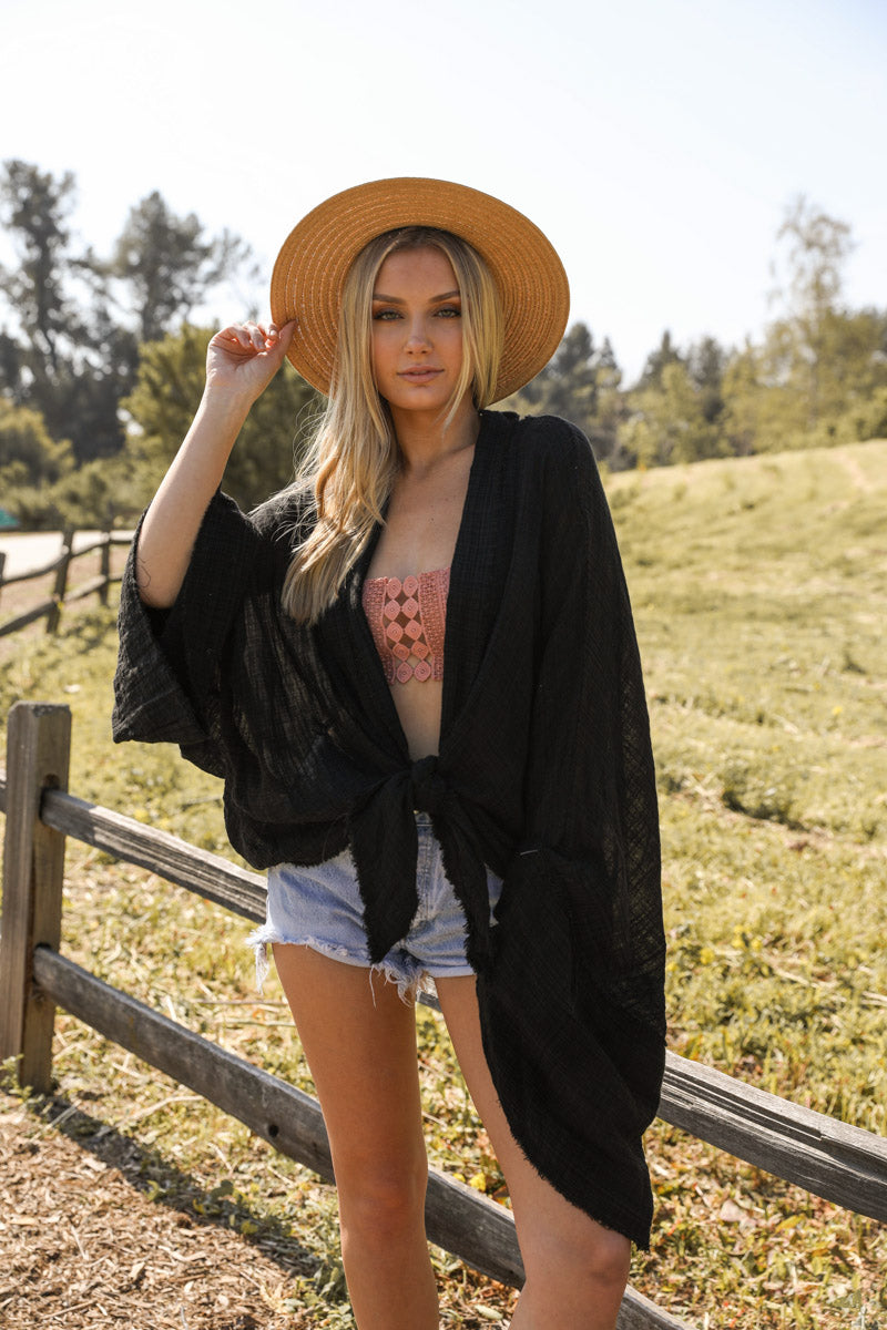 Black flounce tie-front kimono wrap accessory by Periwinkle Aether with flowing fabric and decorative tie detail.