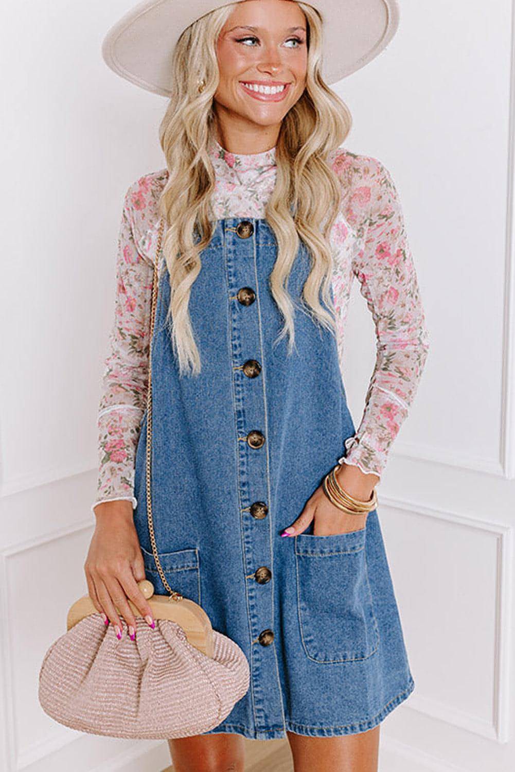 Dusk blue wide strap denim mini dress with button front and front pockets, by Carmine Juneberry, hanging on a rack.