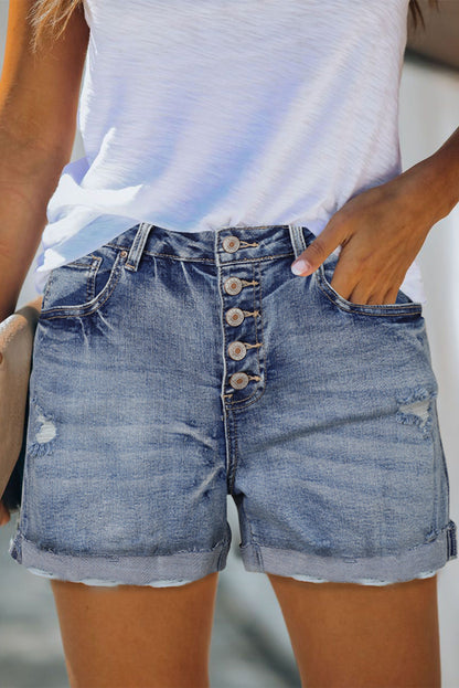 Distressed high rise denim shorts with button fly from Harlequin Daisy, showcasing casual style and frayed hem details.