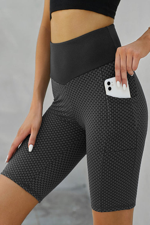 Black ruched yoga shorts with side pockets and butt lifting design by Harlequin Daisy, perfect for active wear and comfortable movement.