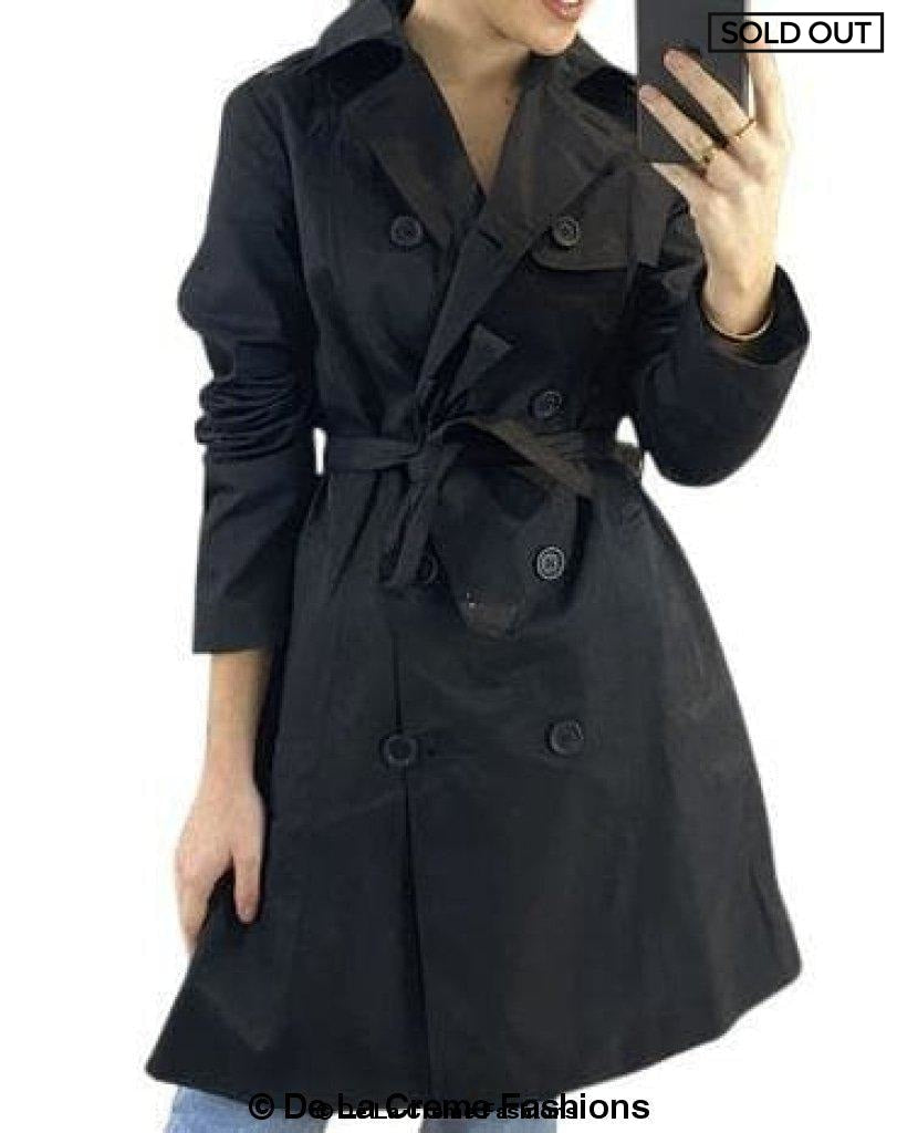 Black cotton blend belted trench coat by Rose Eleusis, shown on a model, featuring classic double-breasted design and waist belt.