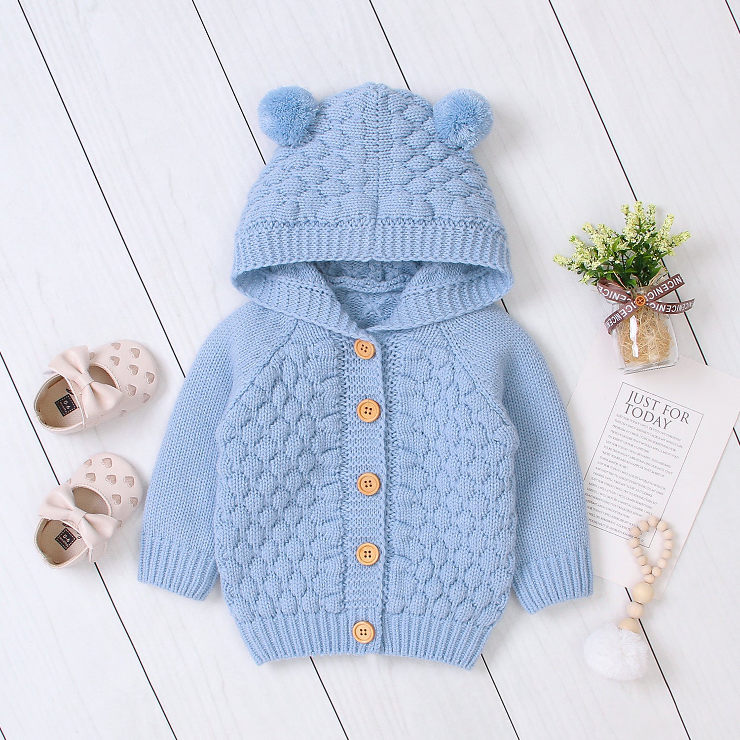Baby wearing Carmine Juneberry KuschelGlöckchen™ hooded knit jacket with pom-pom, cozy baby clothing with a hood and decorative pom-pom.