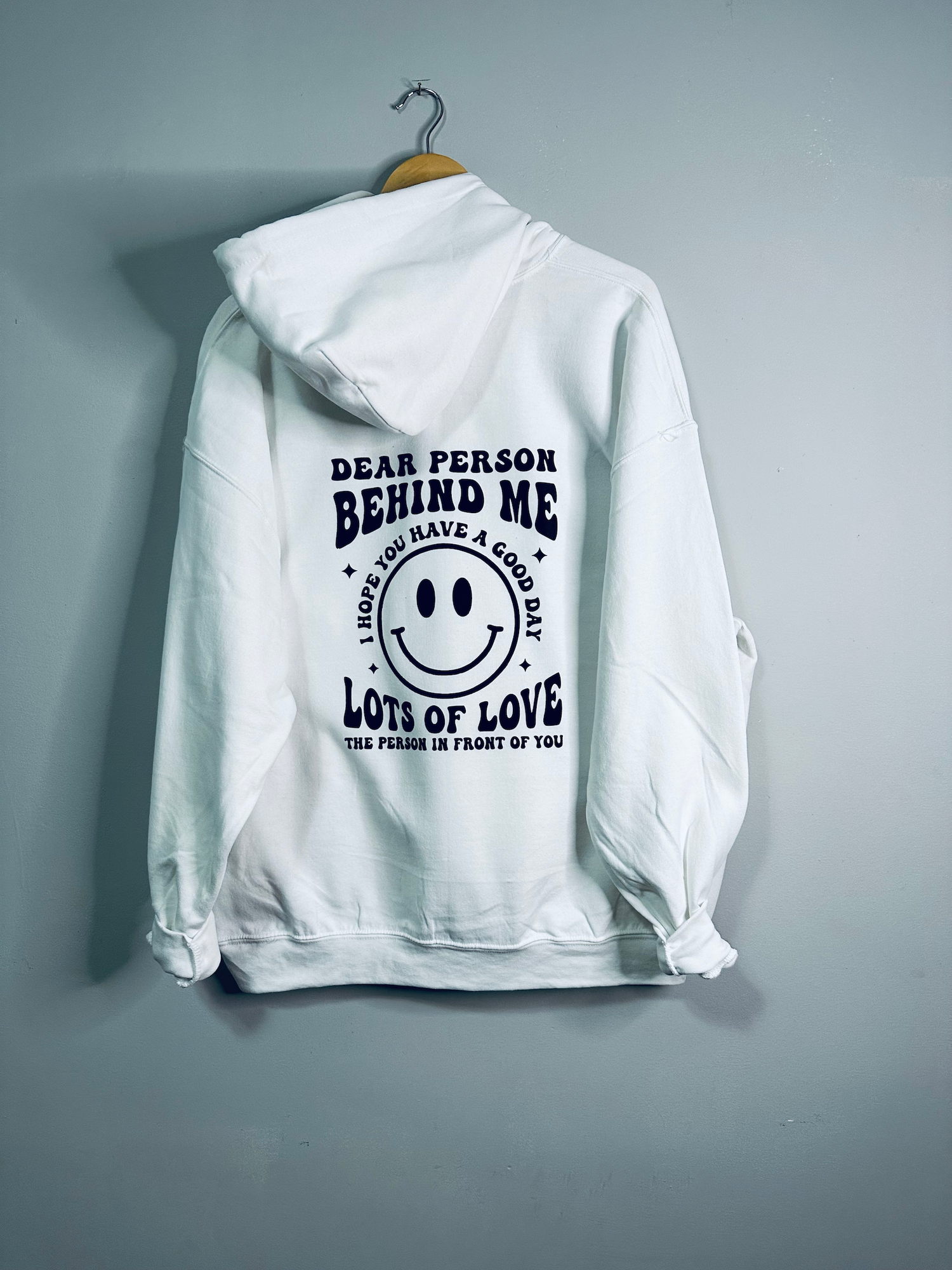 White hoodie from Emerald Ourea with "Dear Person Behind Me" text, casual sweater with a relaxed fit and drawstring hood.