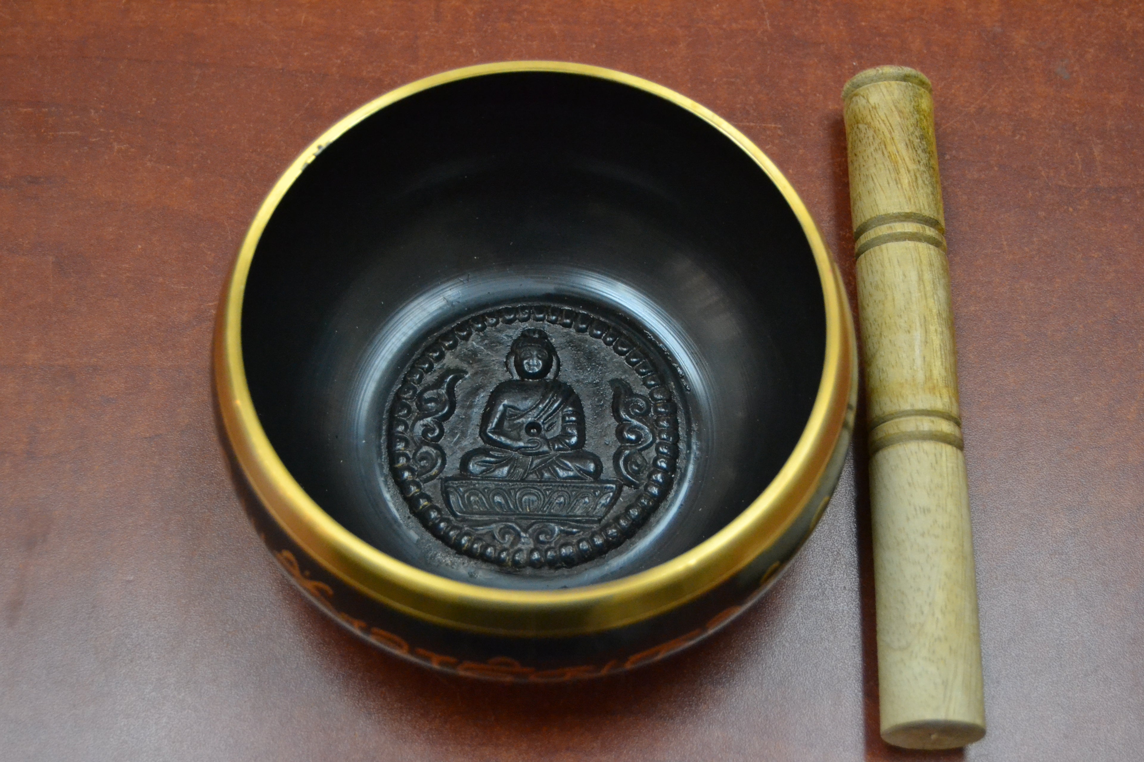 Handmade Nepal Tibetan brass singing bowl from Grey Aphrodite, shown with intricate carvings and a wooden striker on a neutral background.