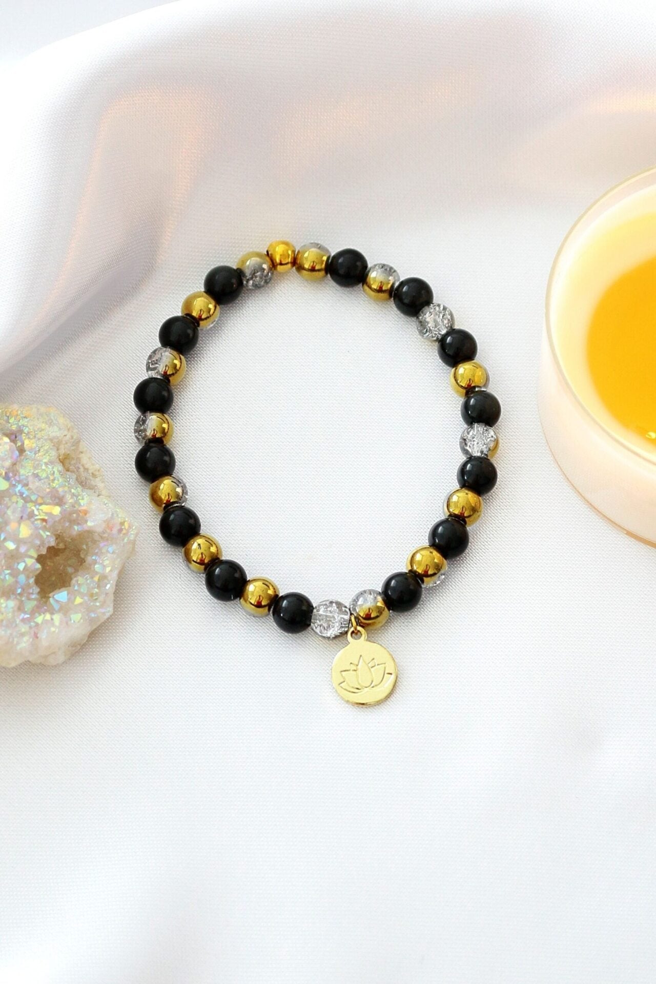 Ultramarine Birch obsidian elastic bracelet with a gold 24K lotus flower charm and adjustable stretch band.