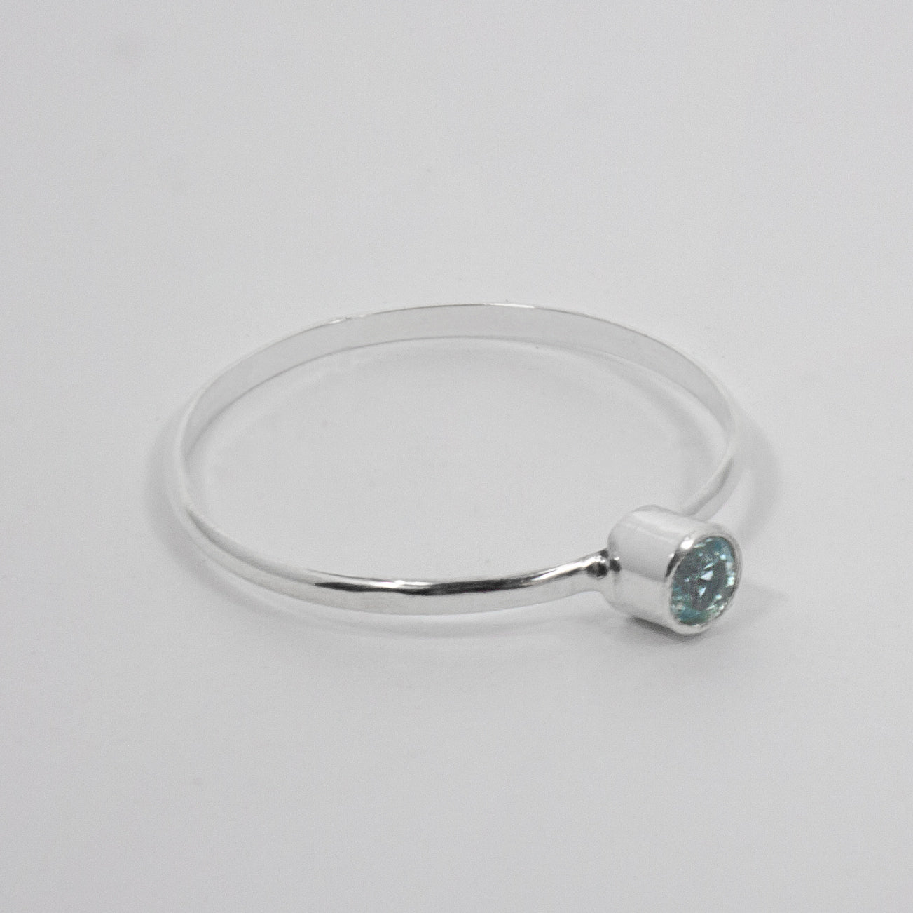 Sterling silver ring featuring a dainty blue topaz solitaire gemstone in a tube setting, elegant jewelry piece by Grey Clymene.